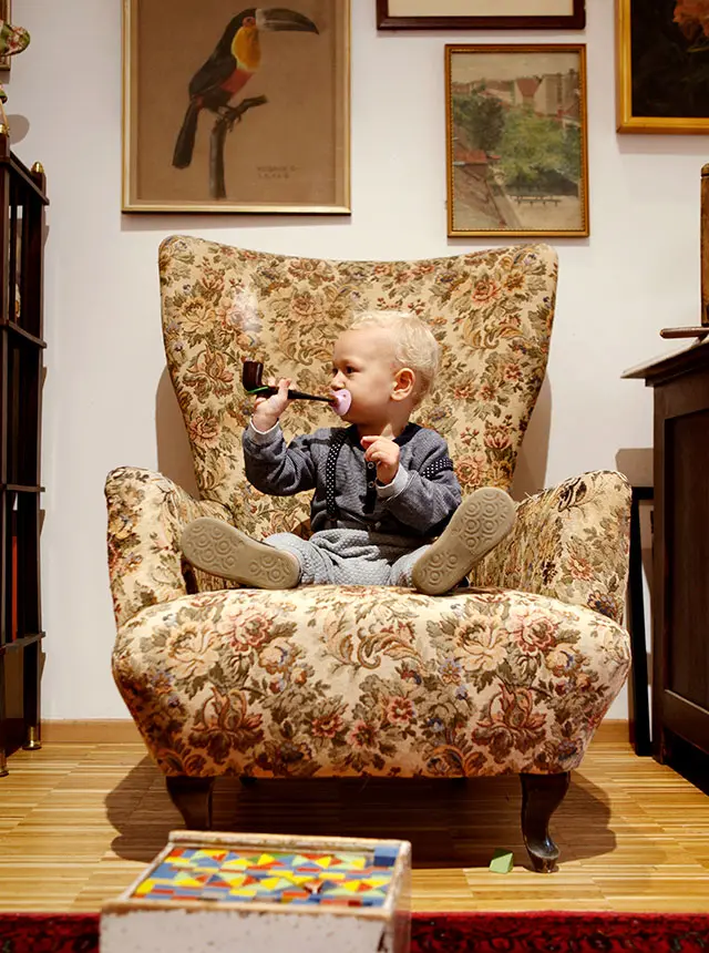 Baby sitzt mit einer Tabakpfeife angemacht an einem Schnuller auf einem älteren Sofasessel - Ausflugsziele im Weinviertel